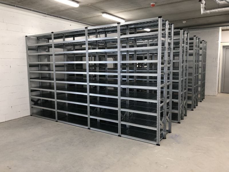 vier rijen legbordstelling in een opslag met witte muren en betonnen vloer